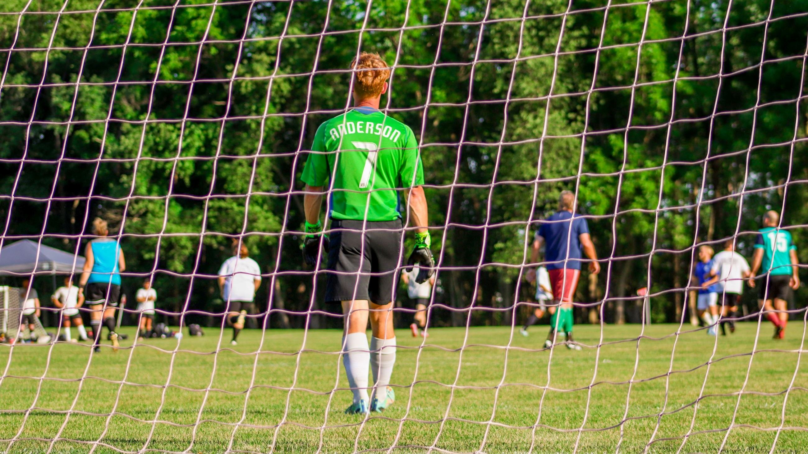 The back of a goalie through a soccer net