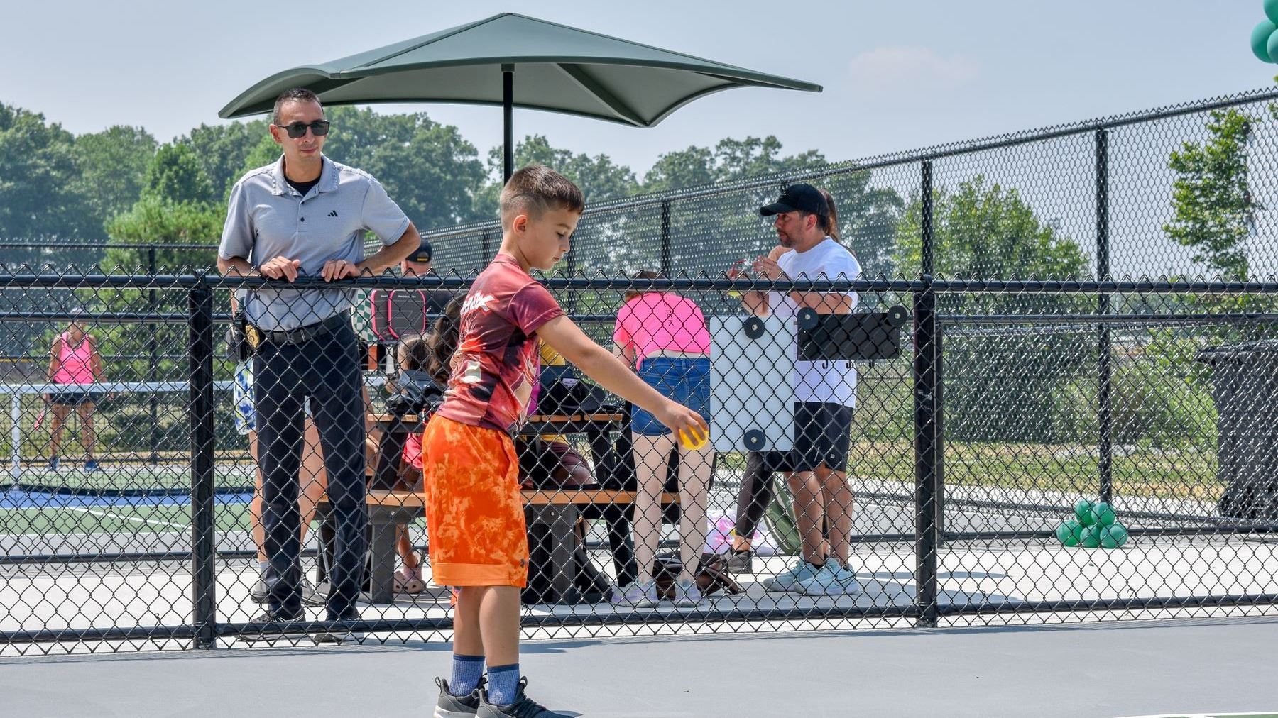 A child getting ready to serve a pickleball while being watched by parent