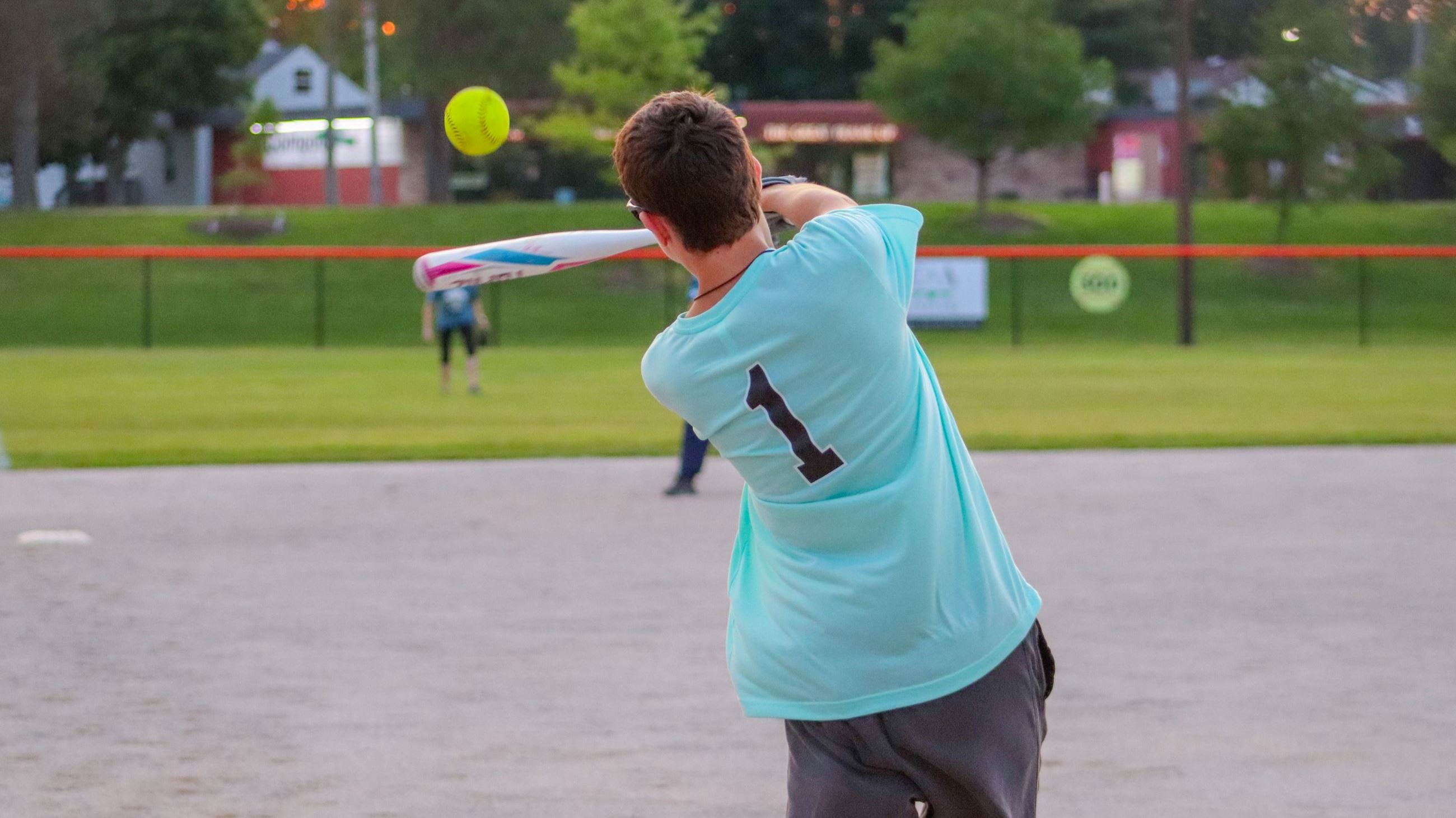 View from behind as an adult swings a bat at a softball