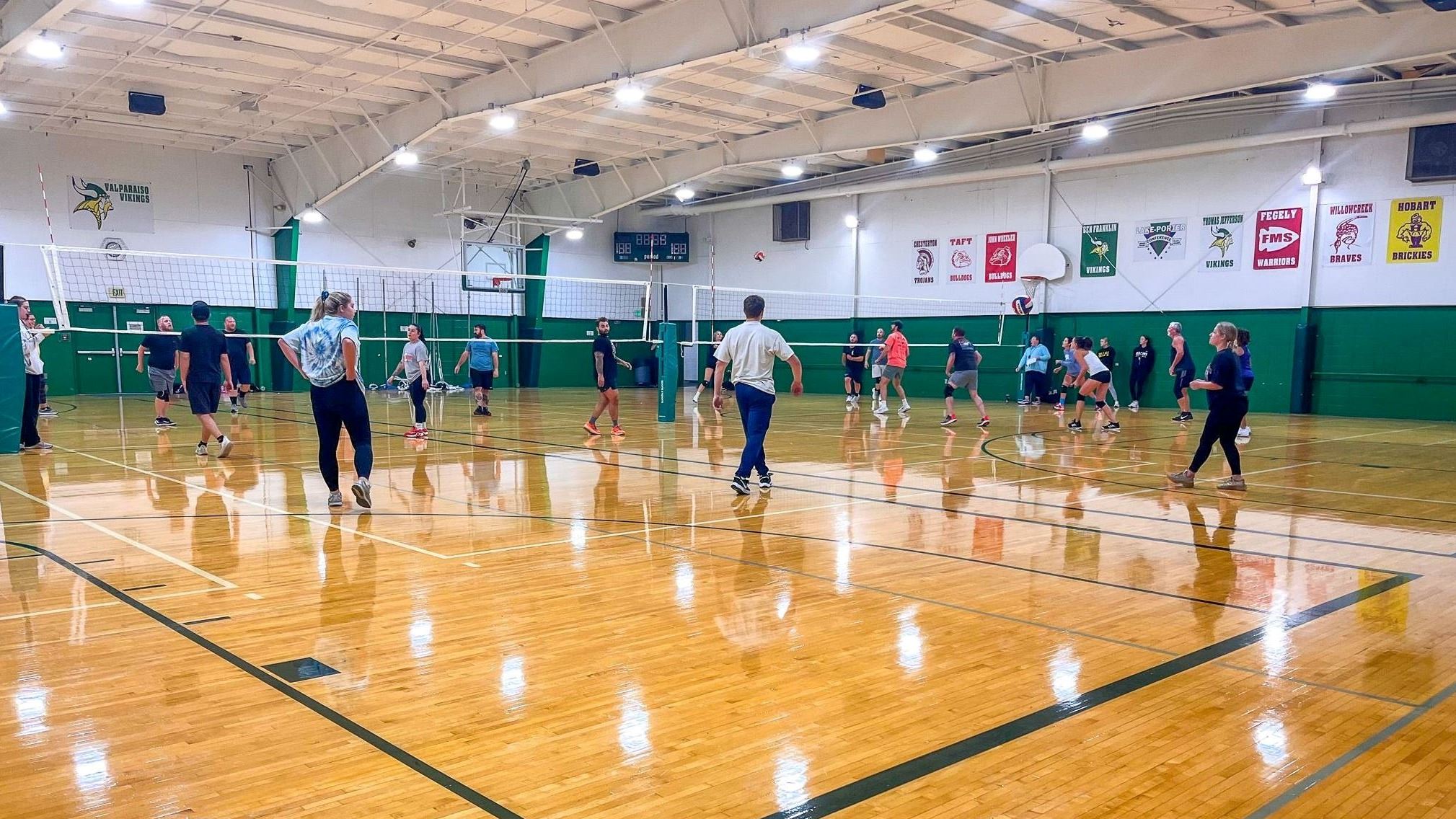 Multiple volleyball courts in a gym with adult players on the courts