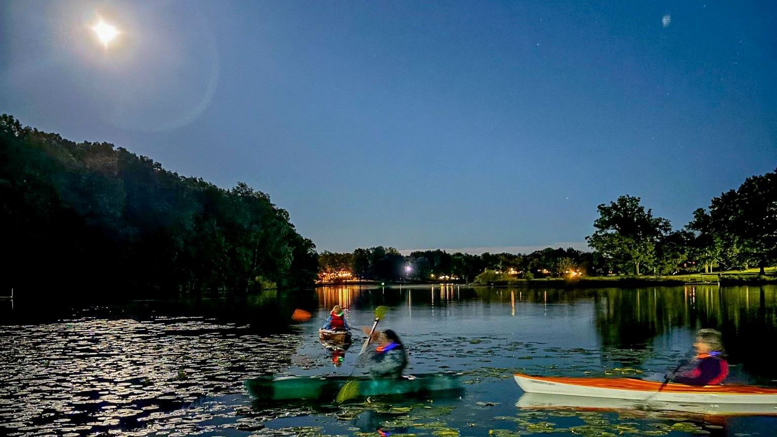 Kayakers on a lake under the moon
