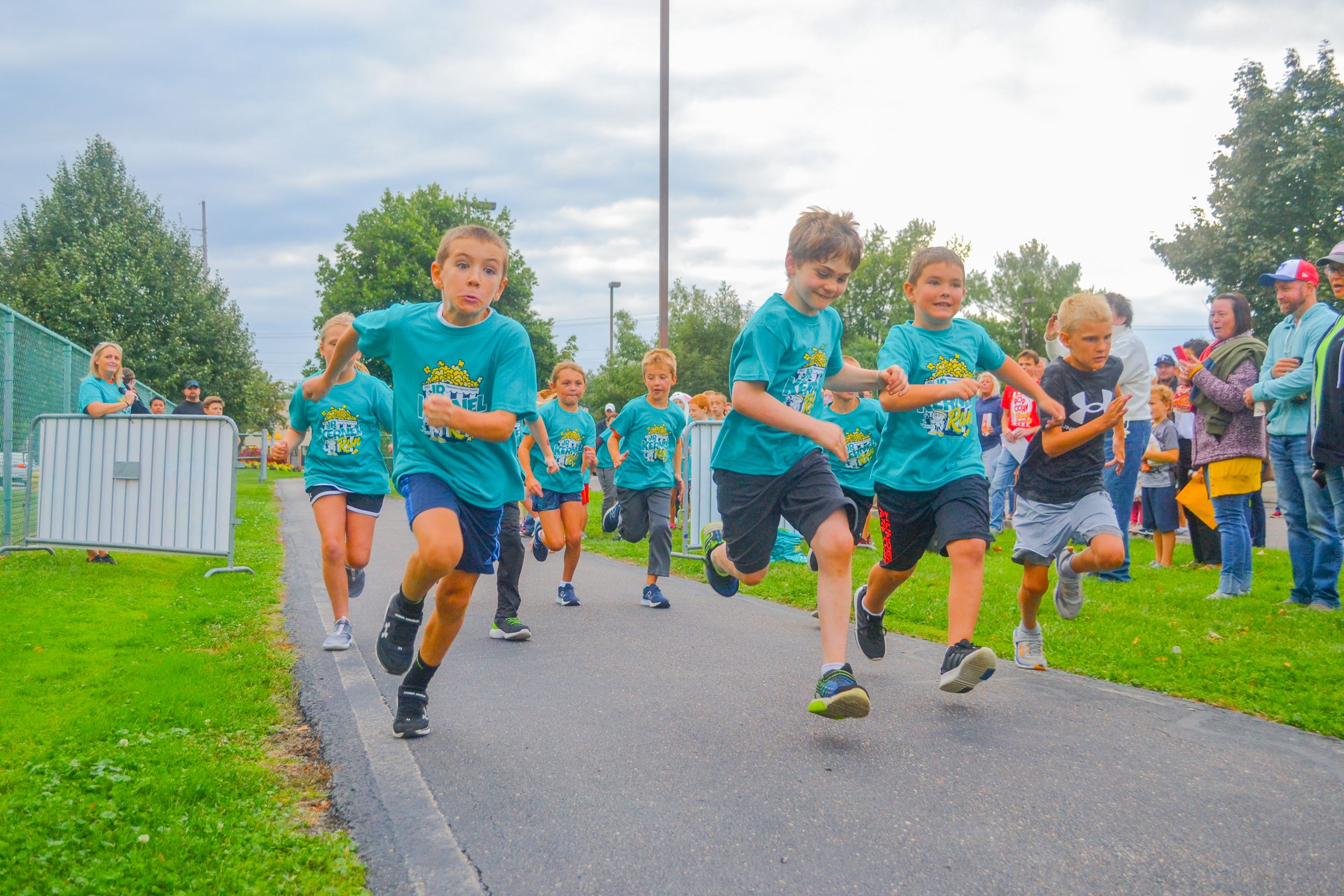 Kids racing on a path wearing matching shirts with adults on the sidelines