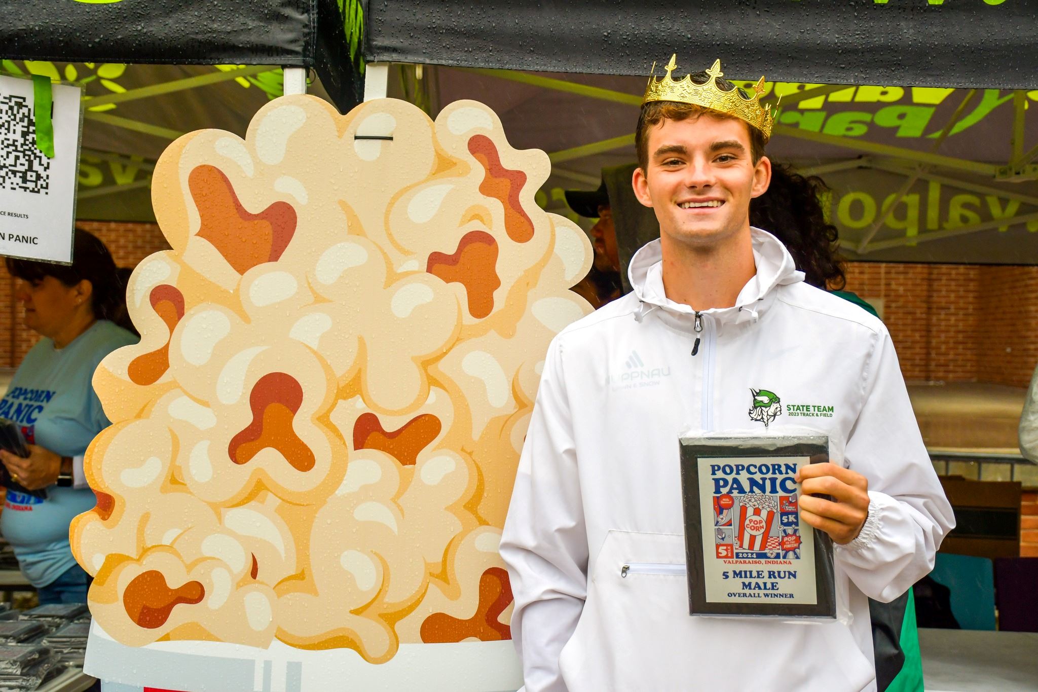 Man holding a plaque and wearing a crown, posing next to cardboard popcorn